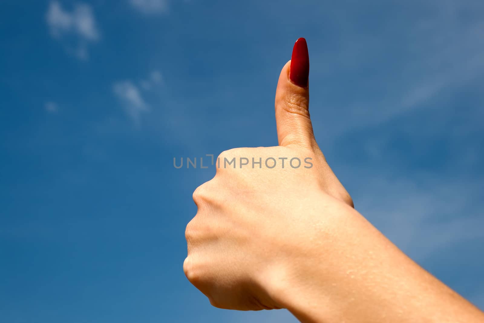 Female hand with thumb up  over blue sky