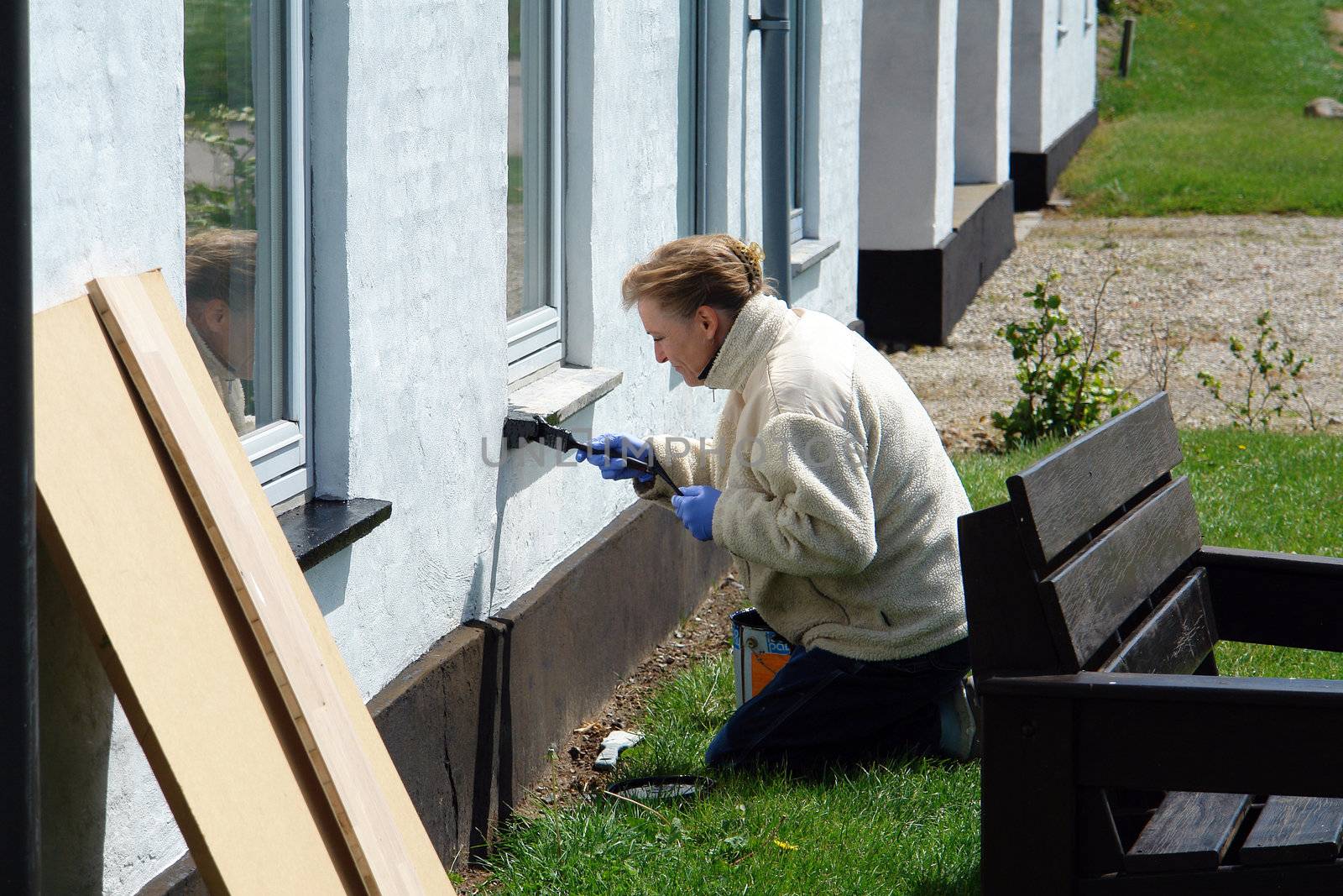 Woman with a paintbrush painting a house during exterior home renovations                            