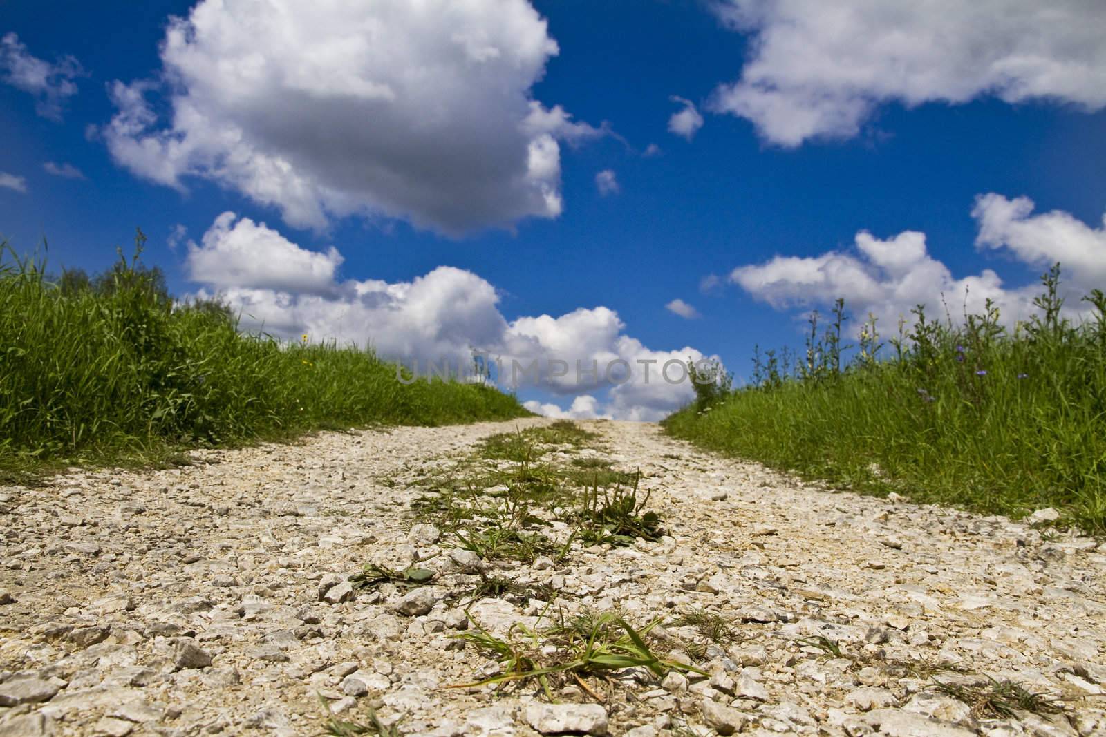 Countryside stone road in fields and blue sky with clouds