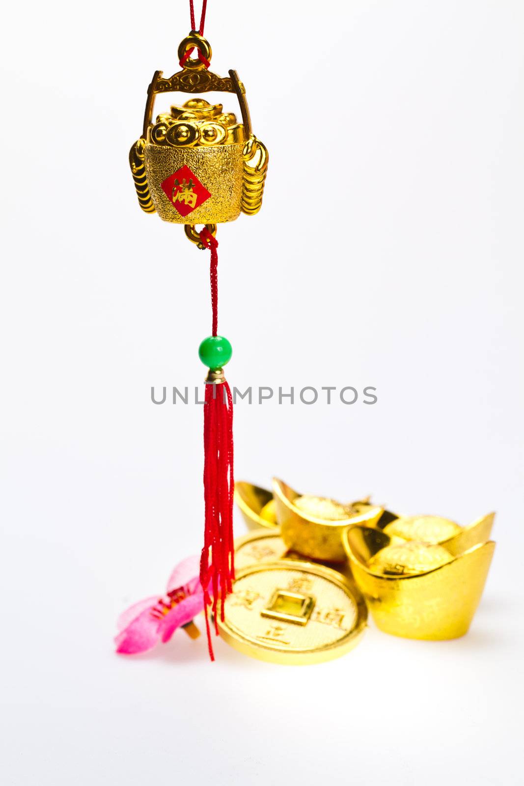 Hanging wealth pot pendant for Chinese New Year celebration with gold ingots and coins in background against white surface