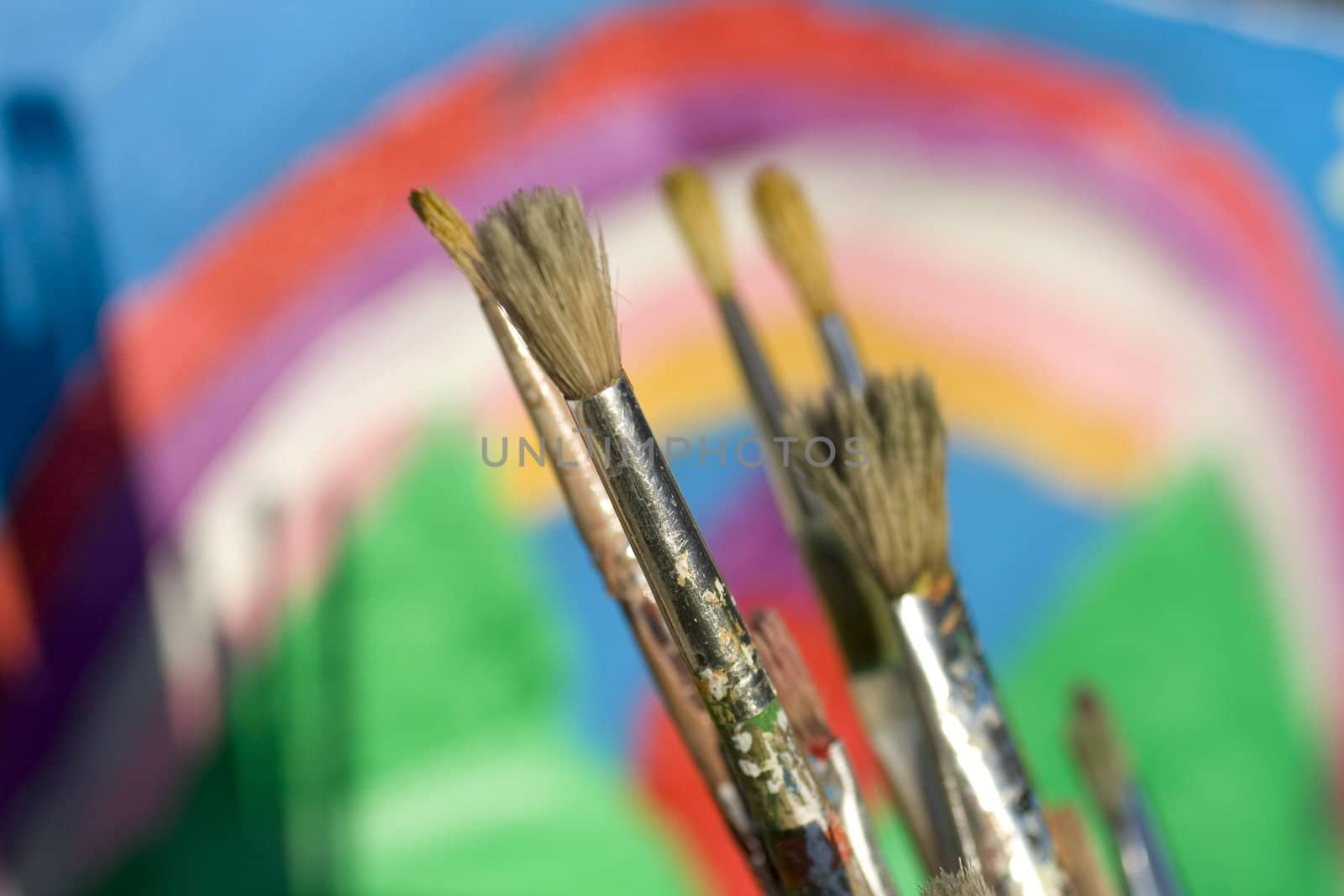 Paintbrushes and painted canvas in the background