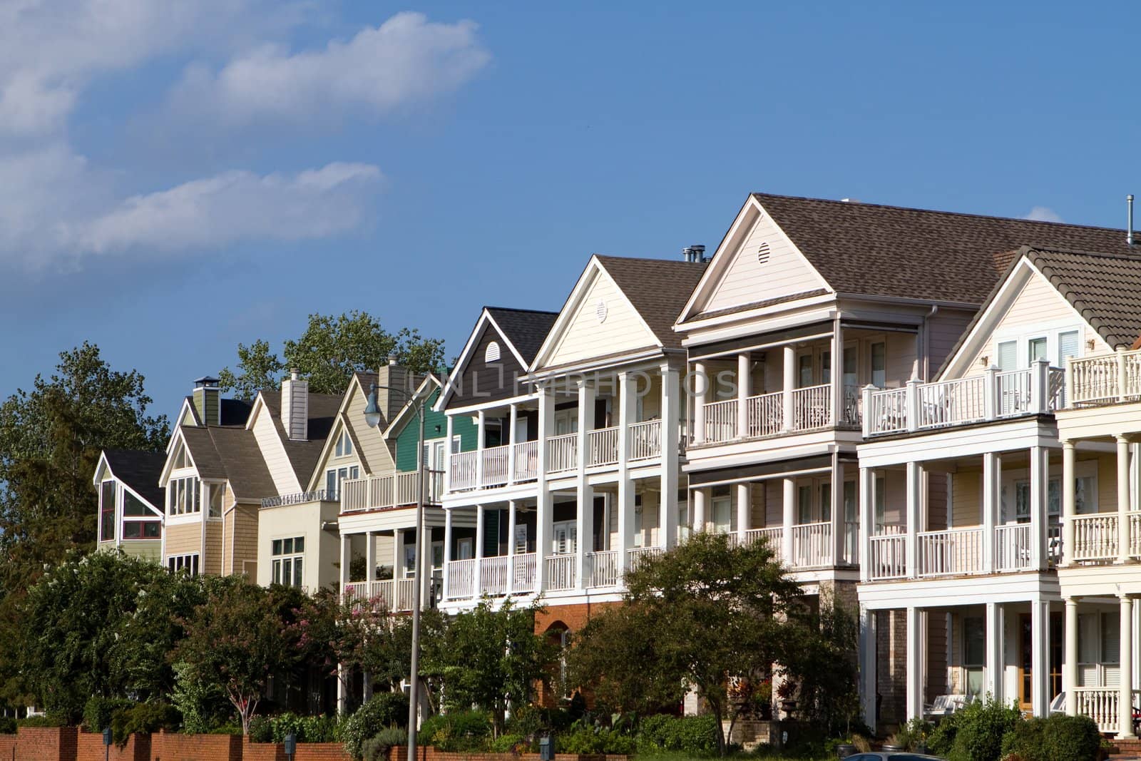 Multi-level high end executive townhomes with porches lines a street against a blue sky.