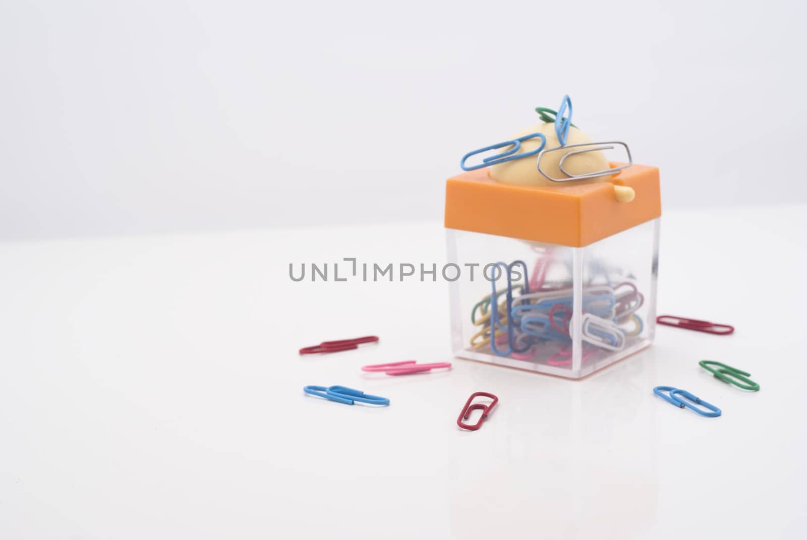 Colorful plastic coated paper clips in clear innovative container with magnet, isolated on white background