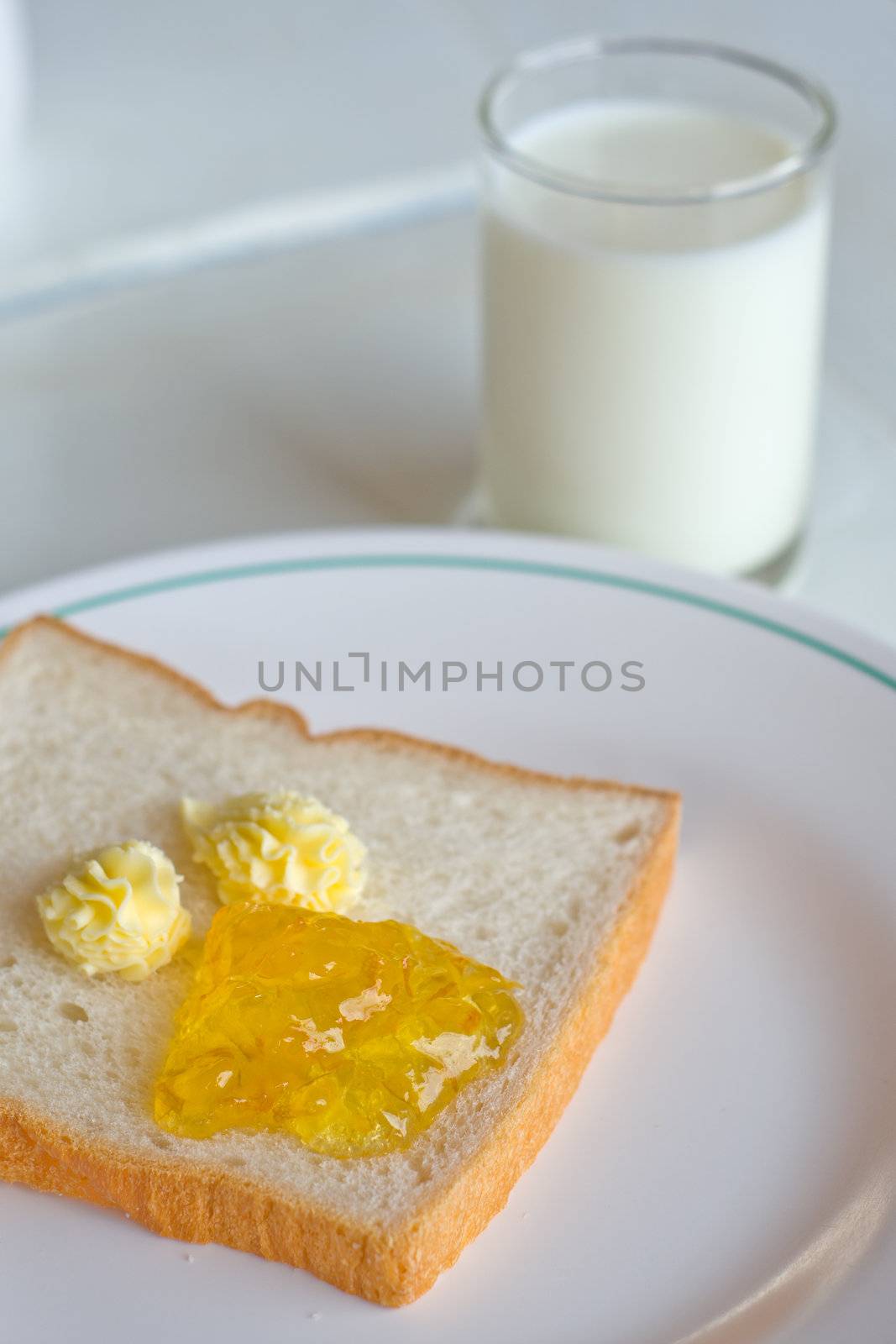 Bread butter jam on white plate with glass of milk