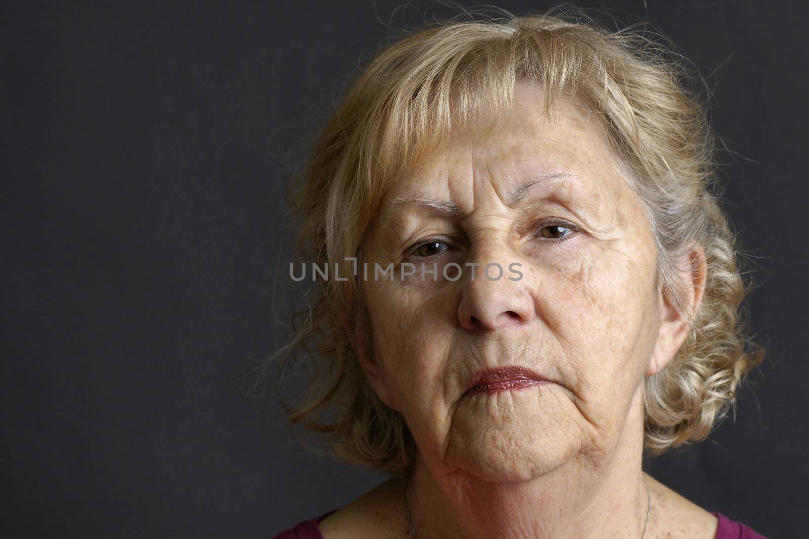 Close-up of a blond senior woman deep in her thoughts over dark background, great details of the aging skin.