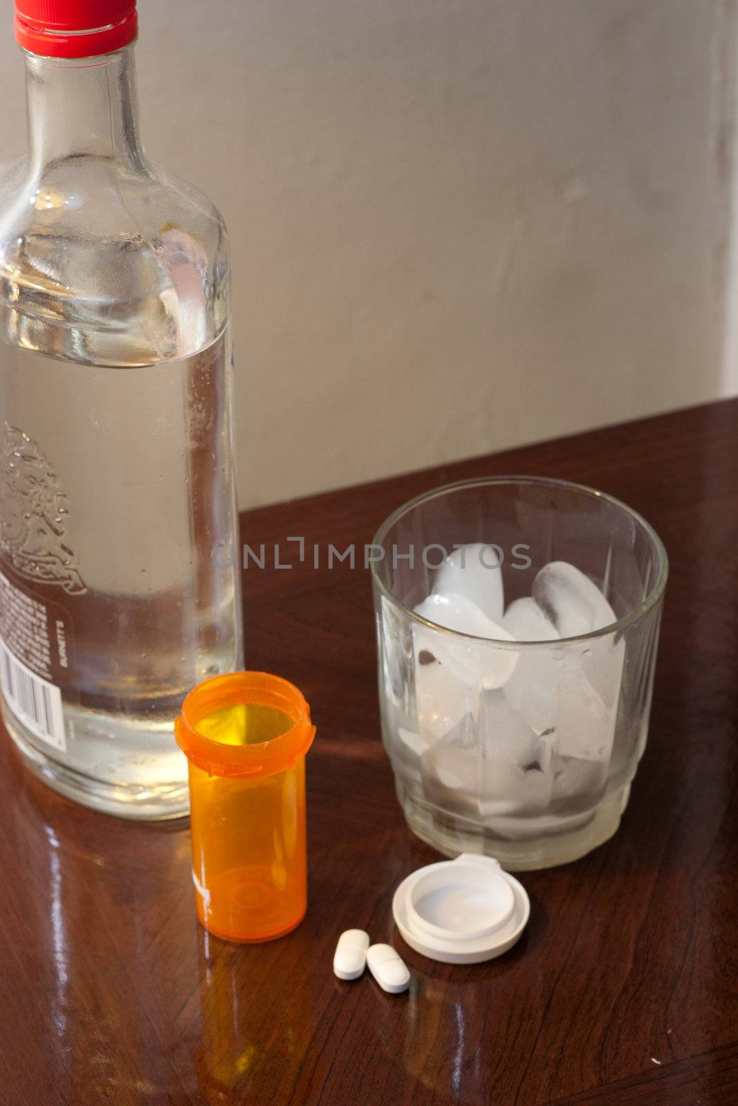 Glass of ice and a liquor bottle with pills and empty bottle.