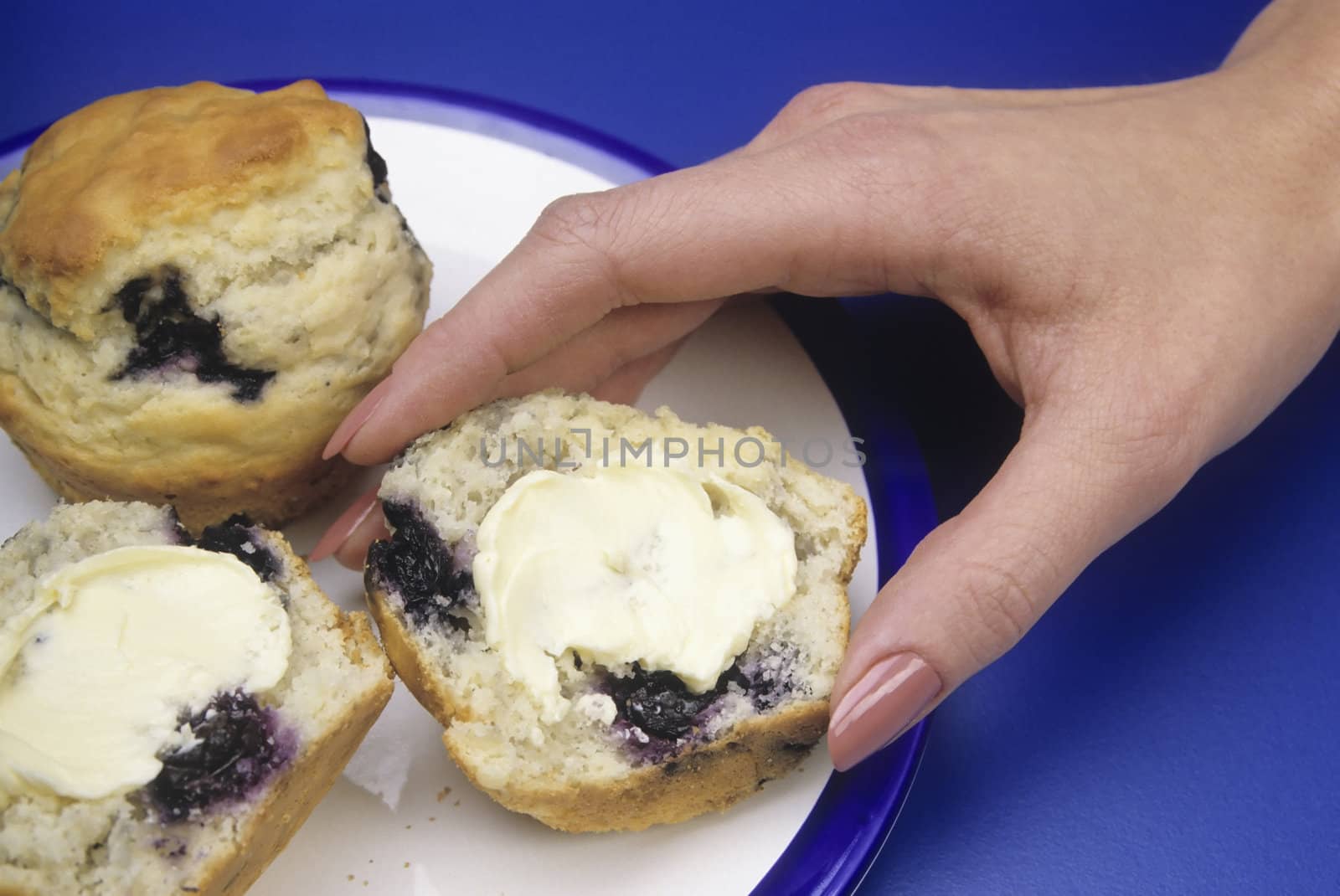 Hand reaching for a buttered blueberry mufin