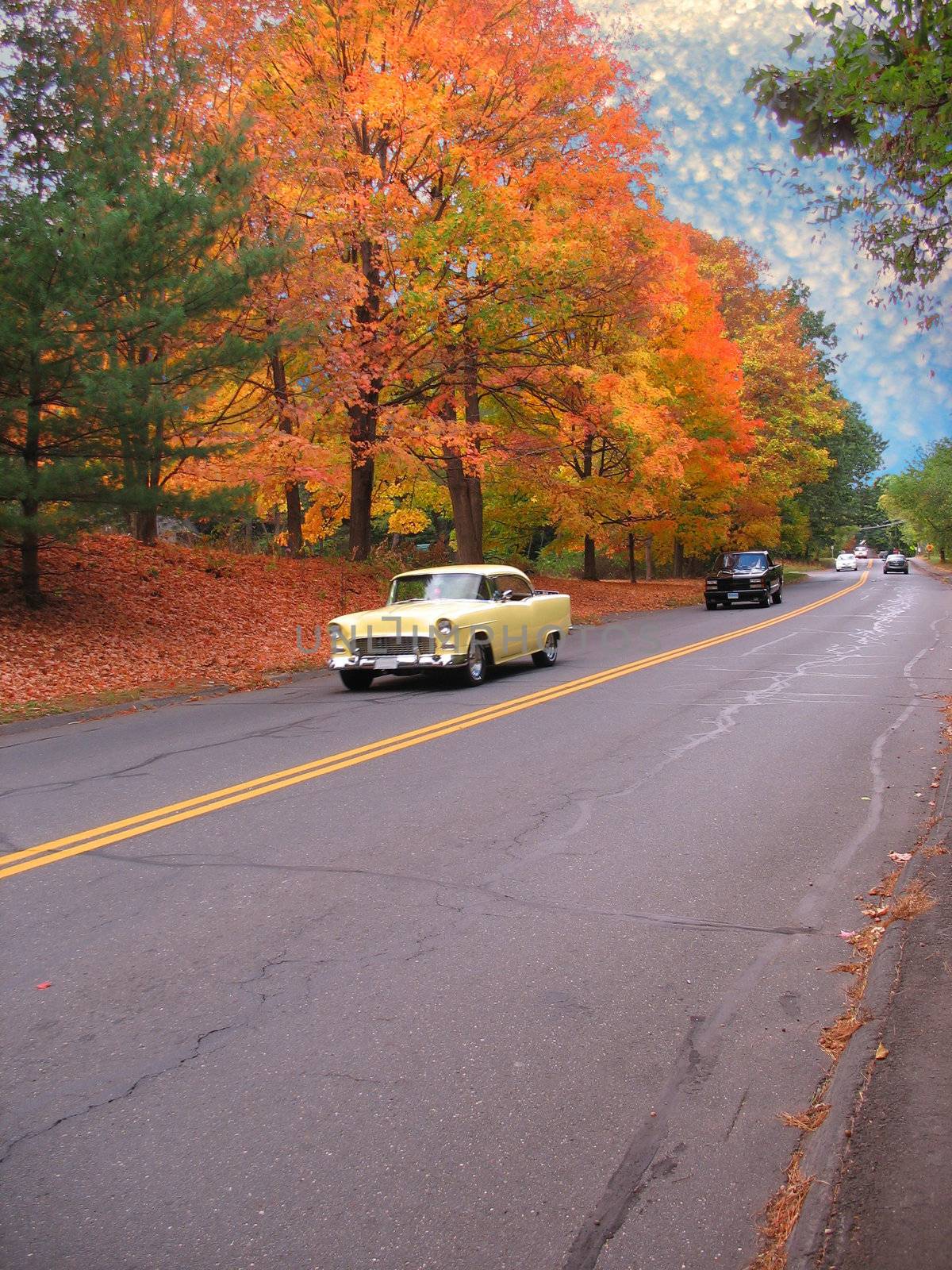A vintage american muscle car driving down the road on a nice autumn day.