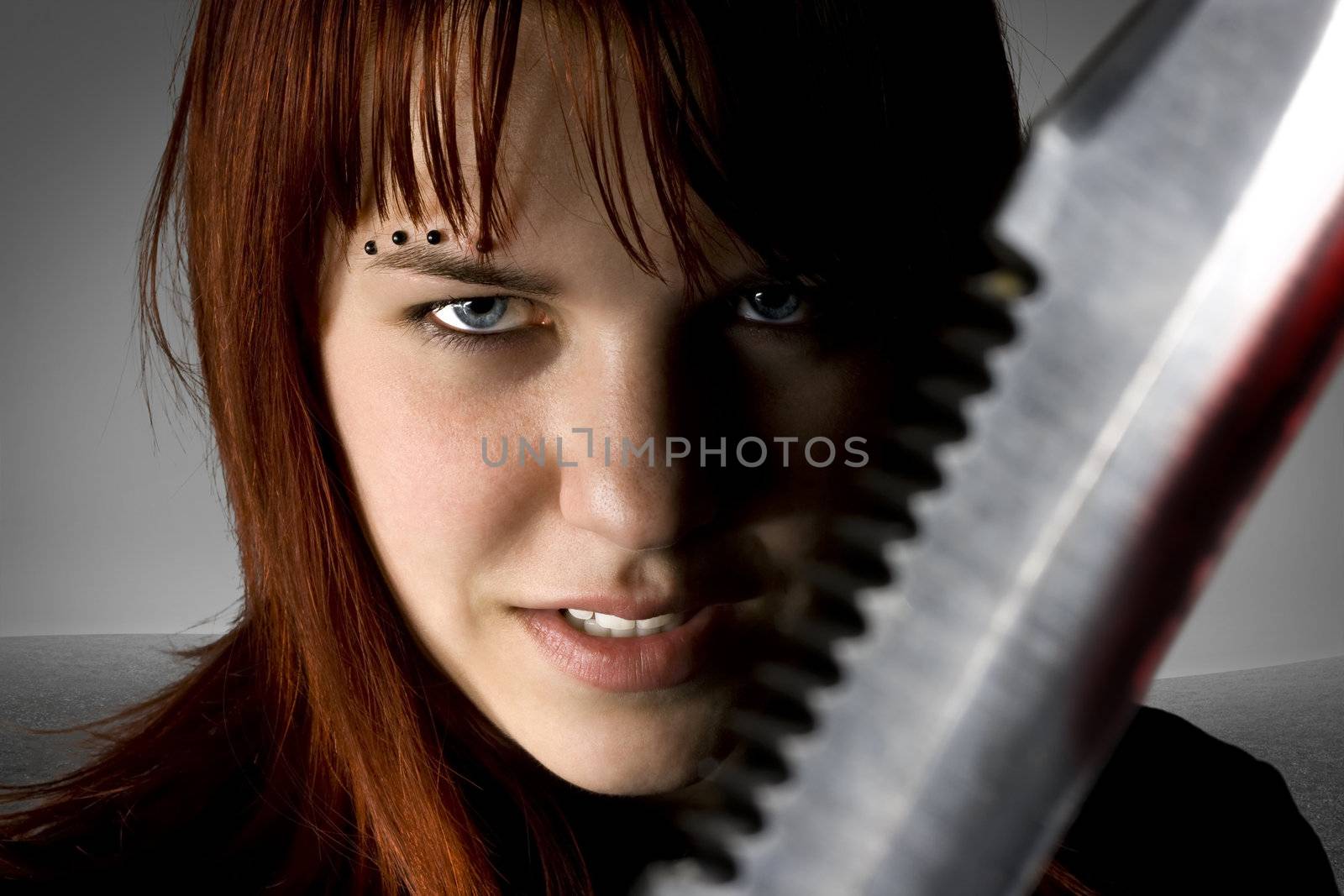 Girl with red hair holding a knife against the camera with an evil smile on her face.

Studio shot.