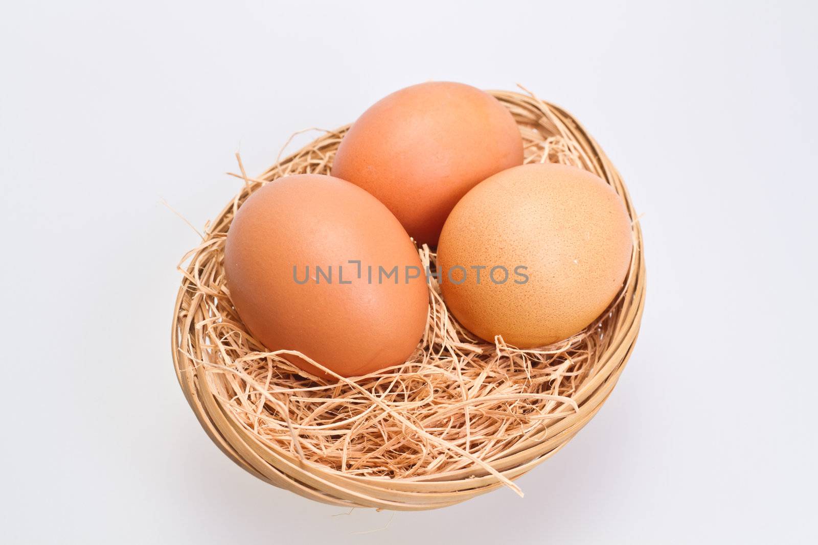 Three brown eggs in rattan basket with straw bedding on white background