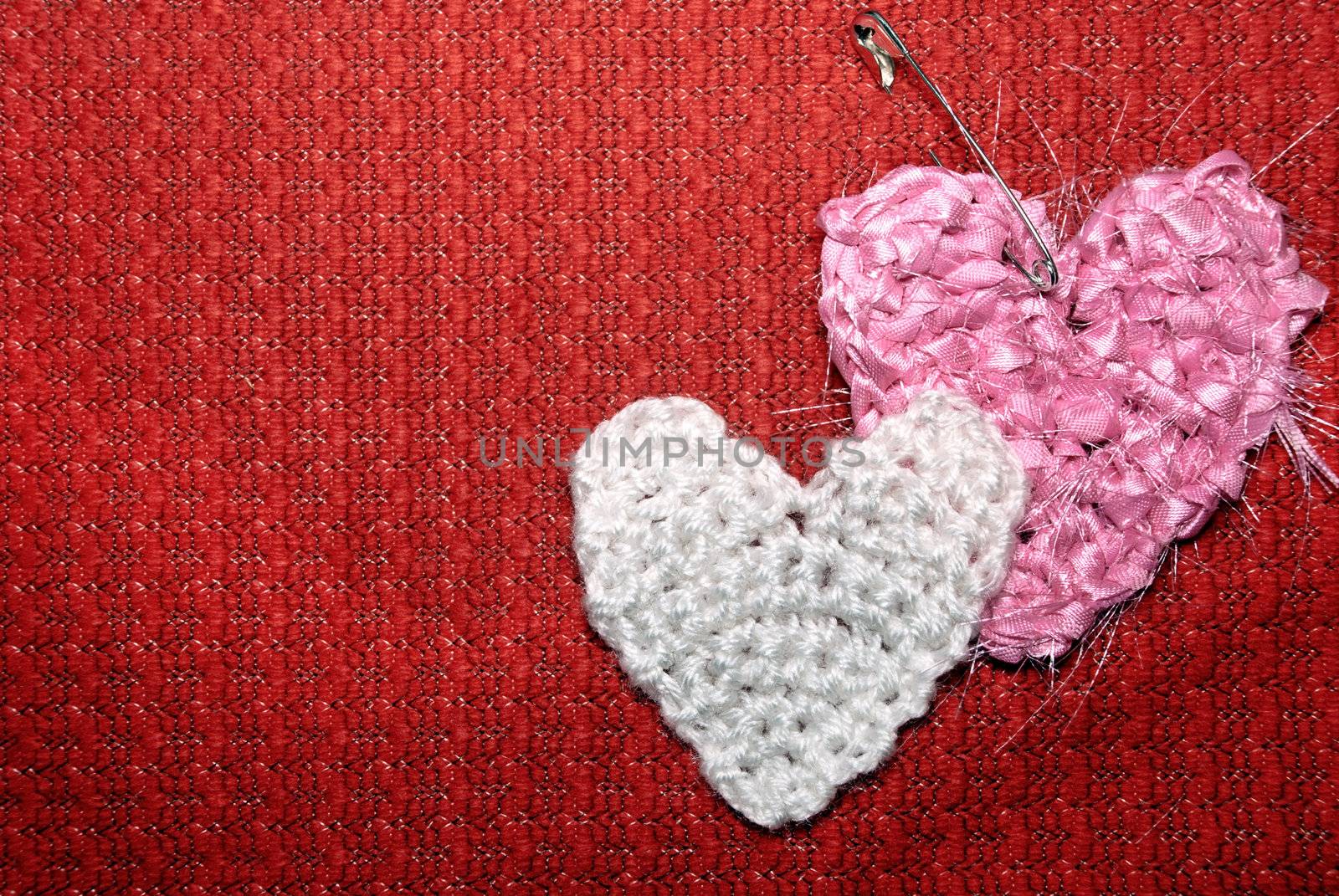 Two hearts on a red knitted textile background.
