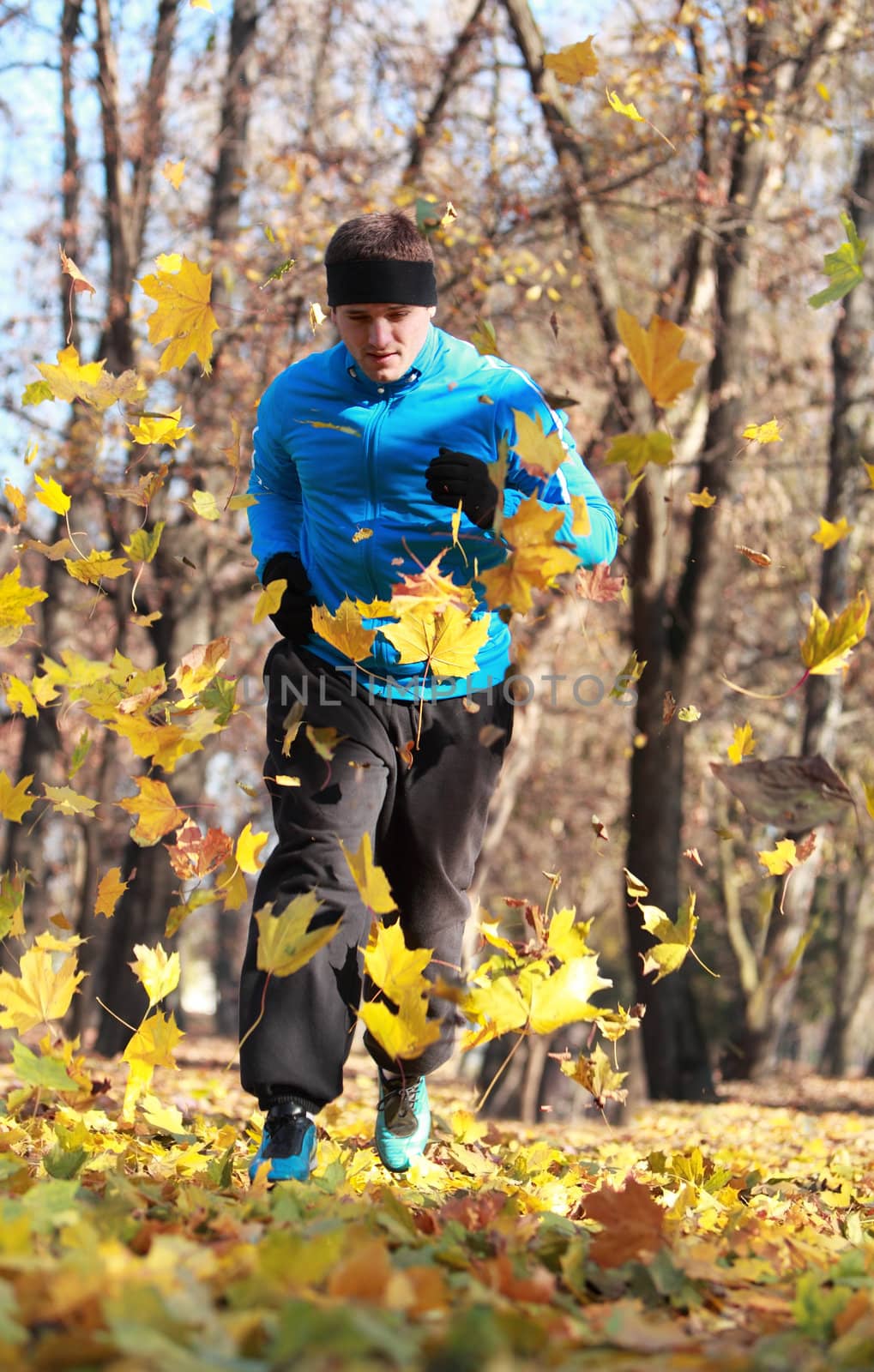 Image of a man running between falling leaves in a park in autumn.