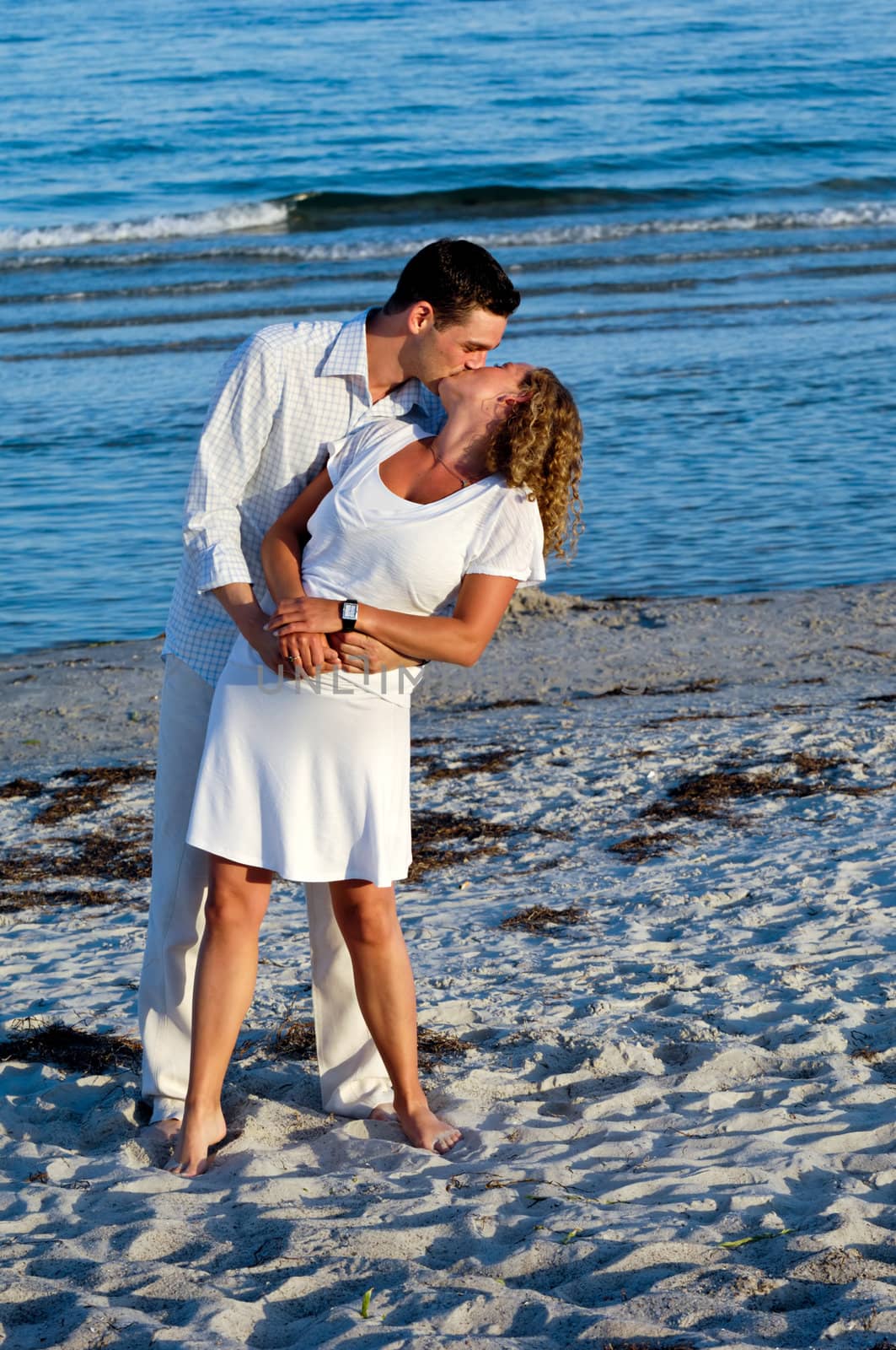 A young couple a standing near beach kissing.