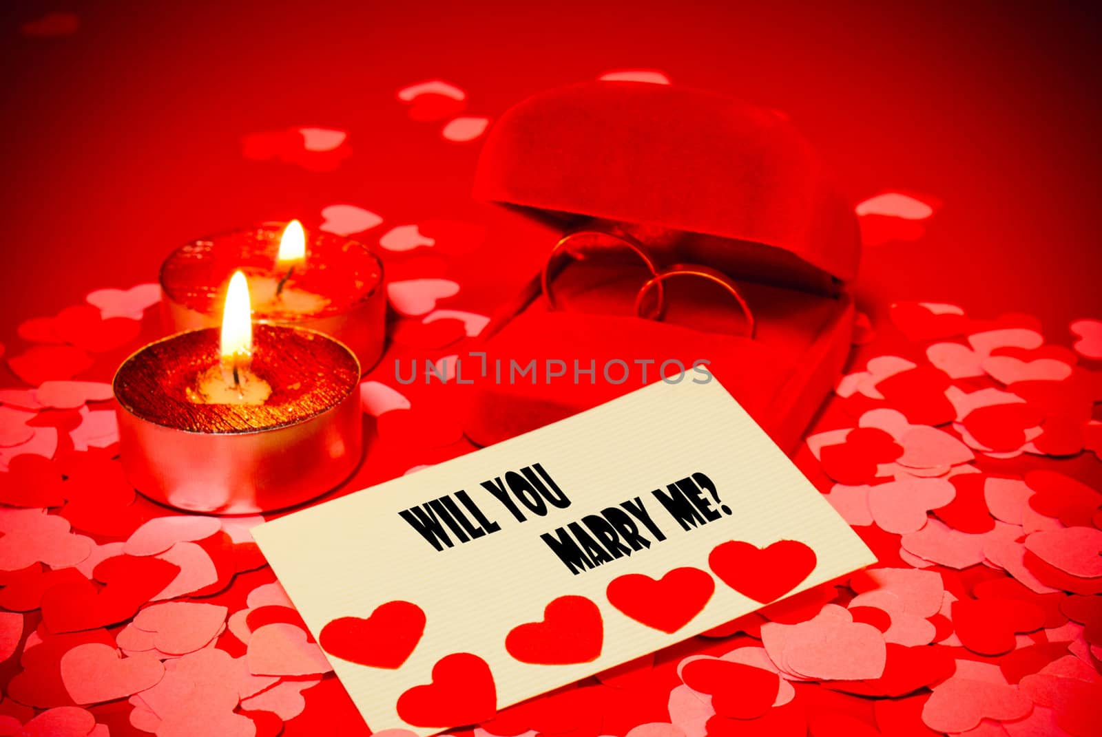 Card with marriage proposal and two rings and two candles over red background