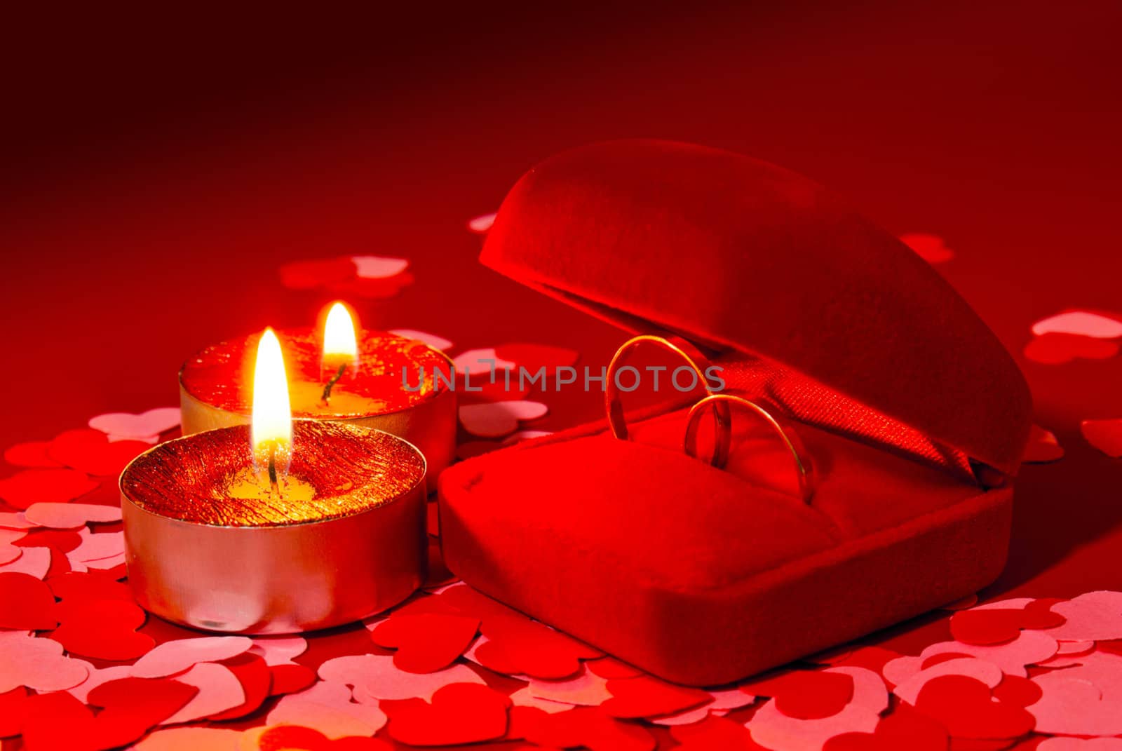 Two rings in a box and two candles over red background