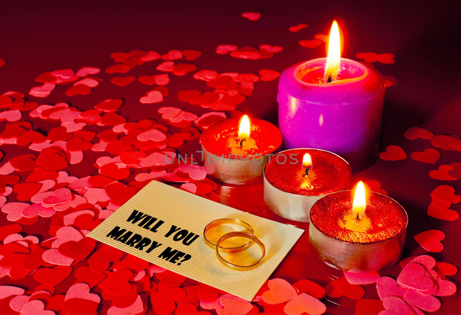 Two rings and a card with marriage proposal with four candles on the red background