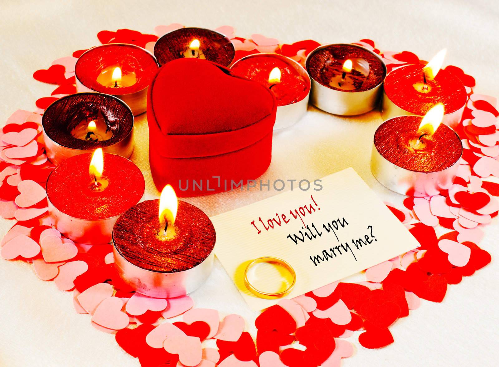 Ring and a card with marriage proposal with burning candles. Shallow depth of field.