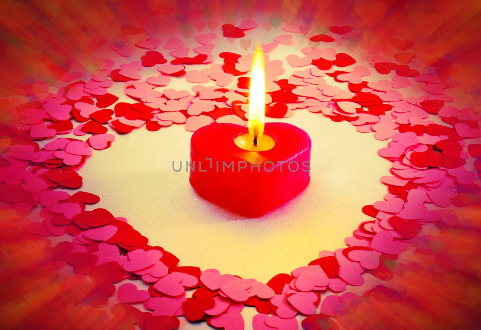 Burning red heart shaped candle over blurry colorful background