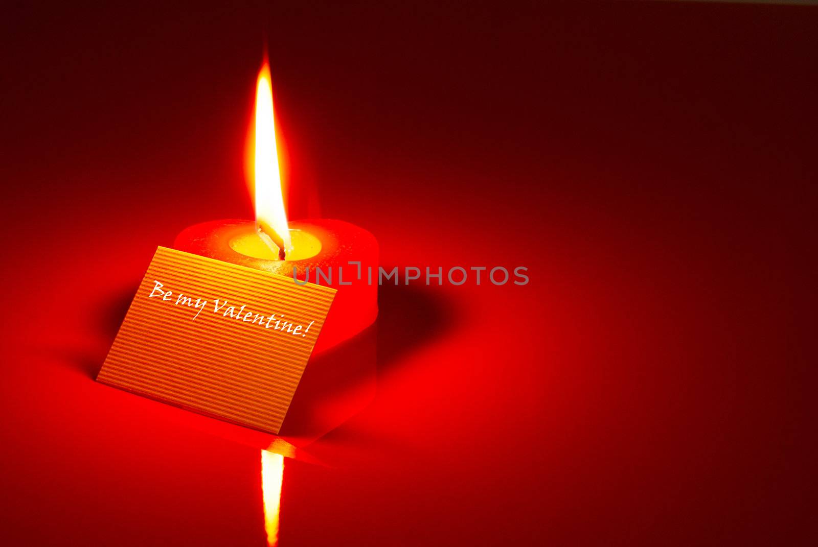 Burning heart shaped candle and a Valentine's card over red background