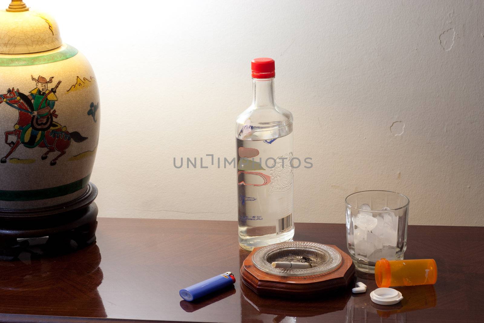 Pills, glass with ice and liquor bottle on coffee table ready to party