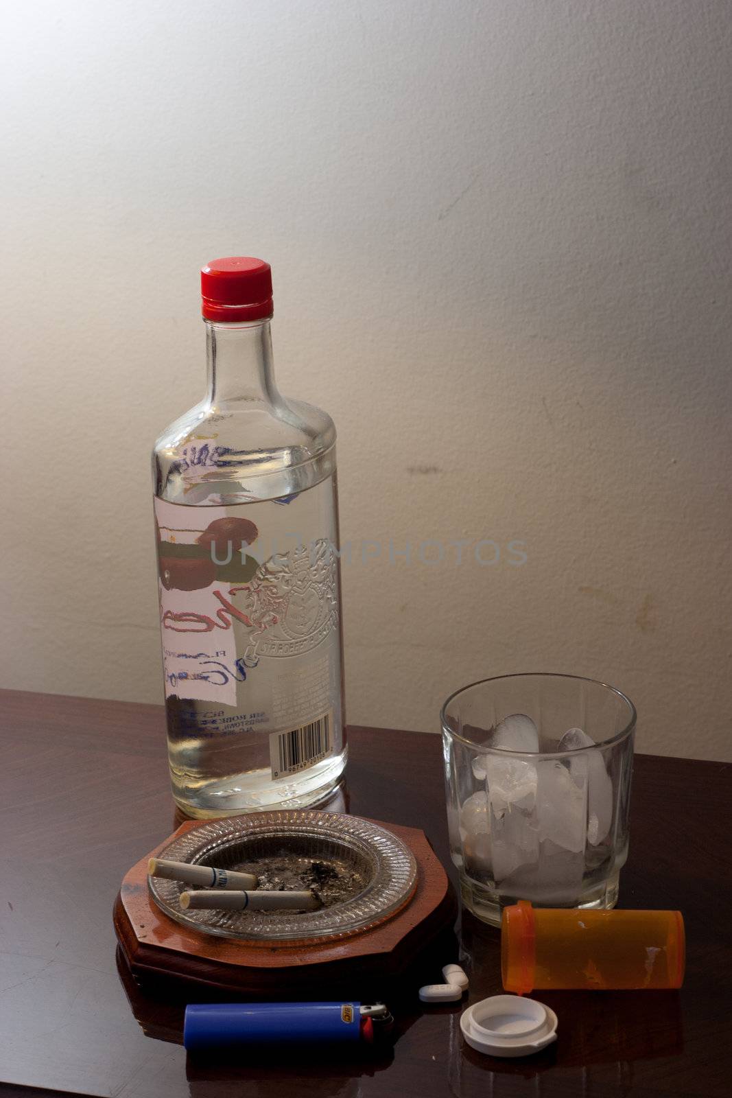 Pills, glass with ice and liquor bottle on coffee table ready to party