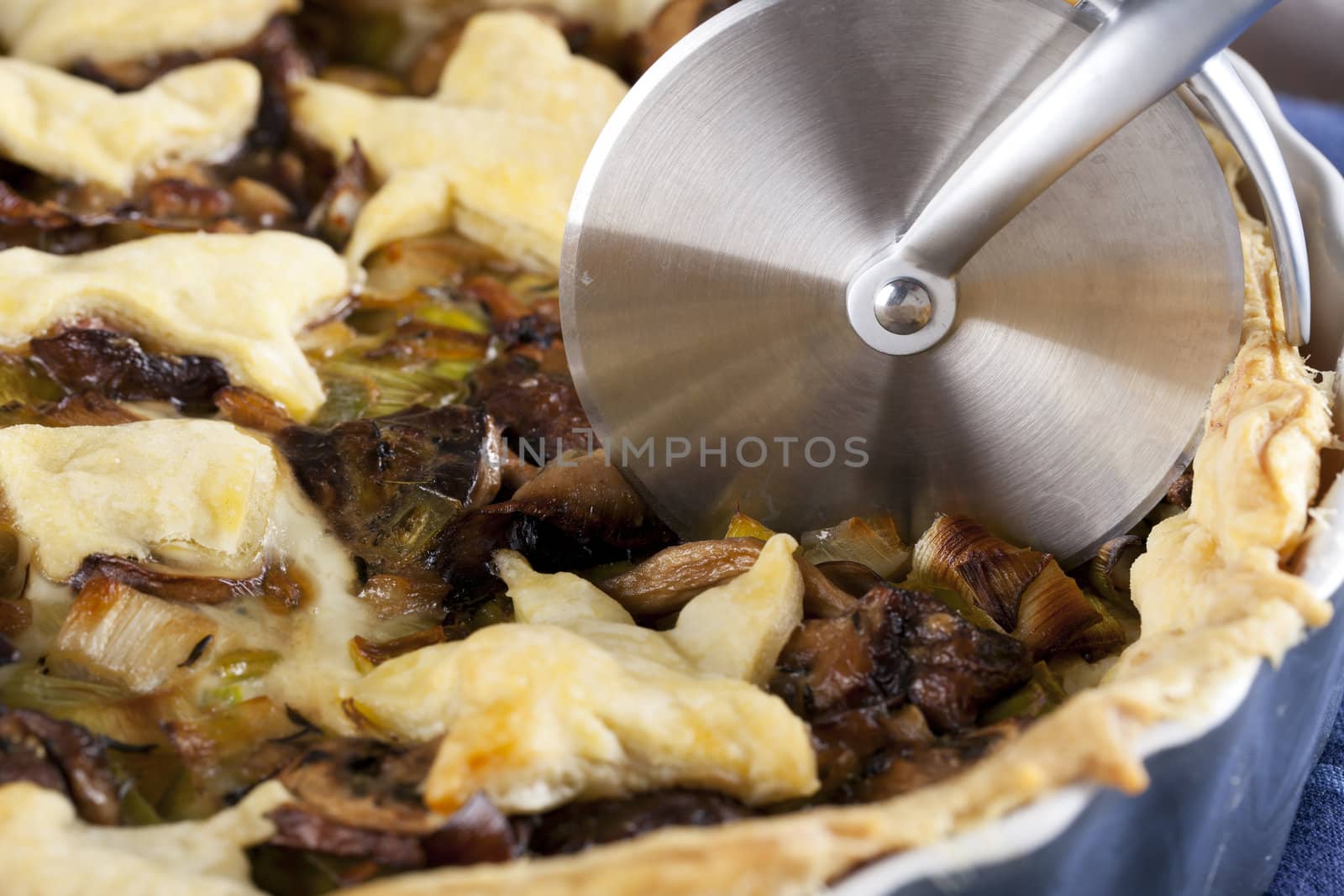 Mushroom and leek tart about to be cut with a pizza cutter.