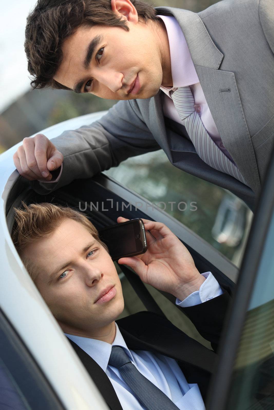 two young businessmen sitting in a car and talking on a cell phone by phovoir