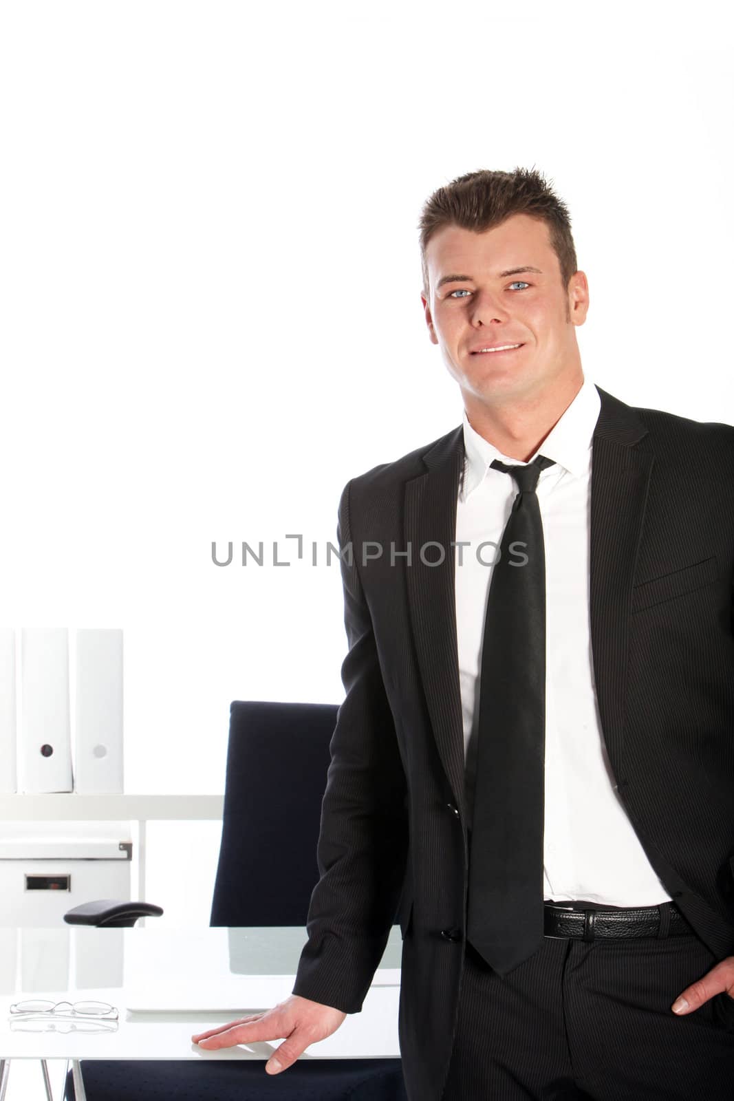 Handsome confident relaxed young businessman standing at his desk with one hand in the pocket of his suit