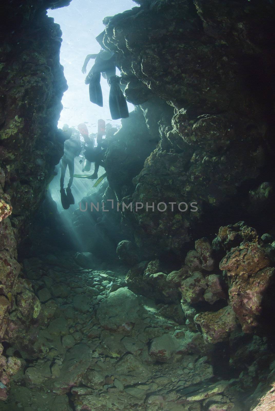 The view of scuba divers swimming through an opening towards sunlight, Dahab, Egypt