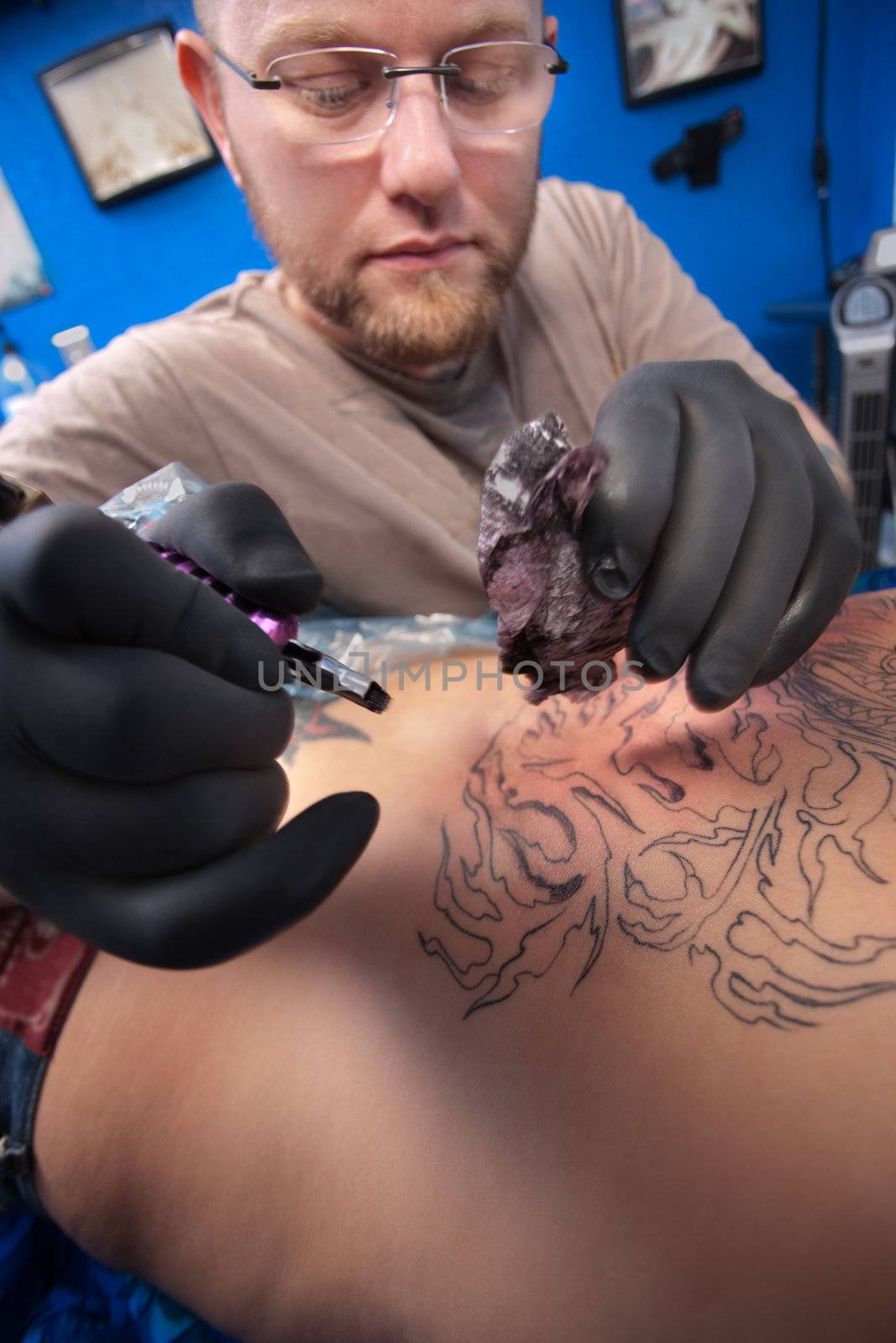 Bearded Caucasian tattooist creates a tattoo on a woman's back