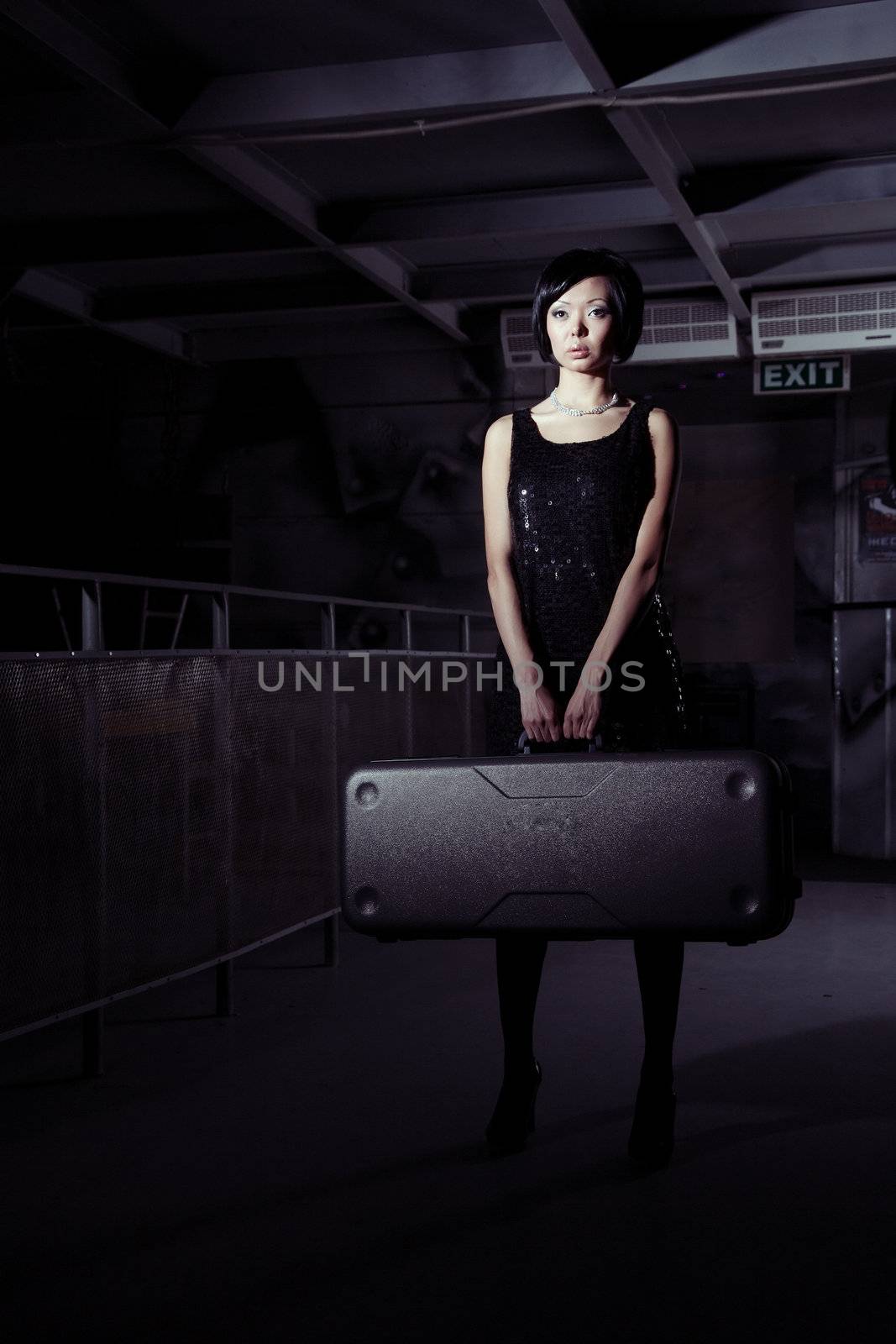 Small brunette lady holding big suitcase in the dark airport terminal