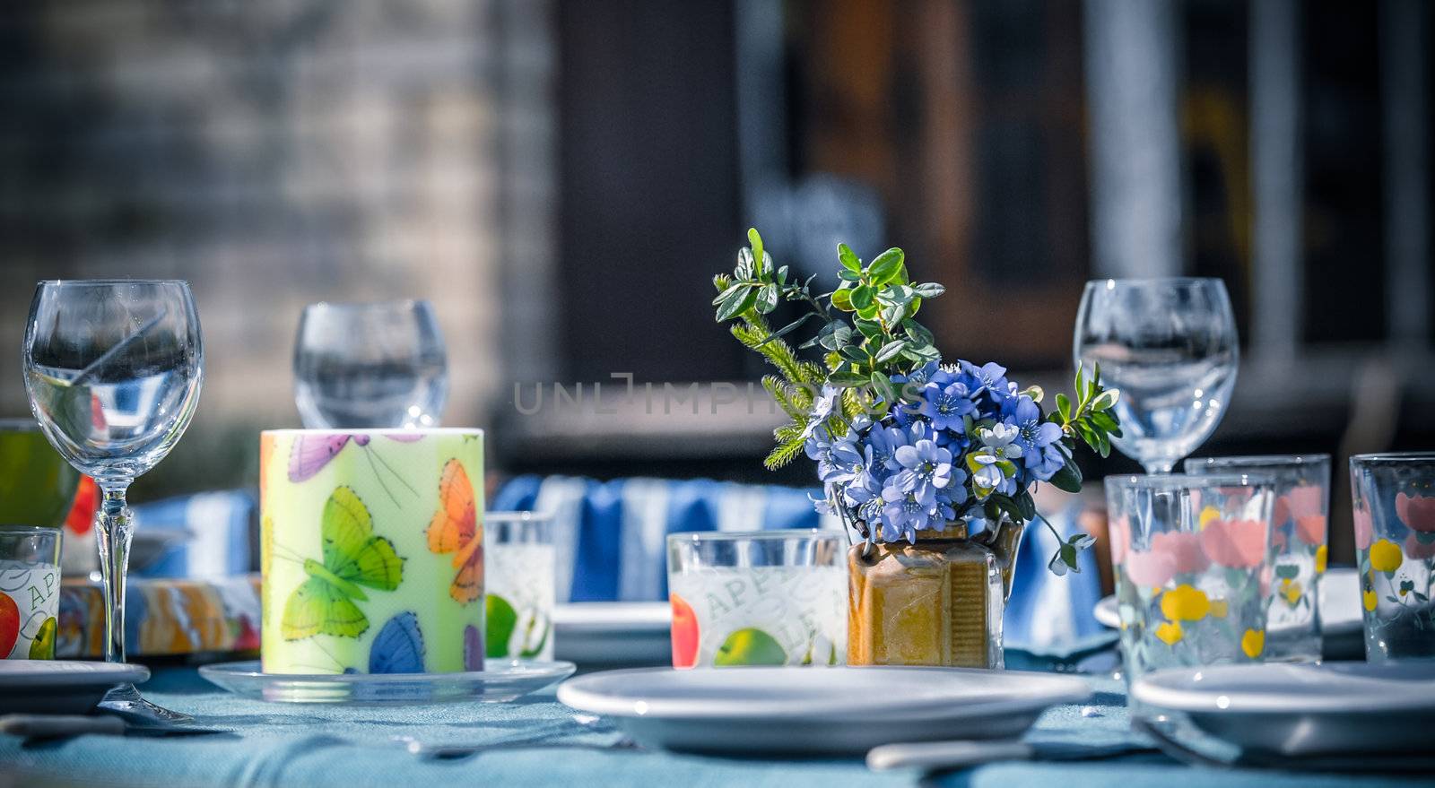 Table set outside for lunch or dinner. The table is decorated with spring flowers and colorful glassware. It is a sunny day in a countryside.