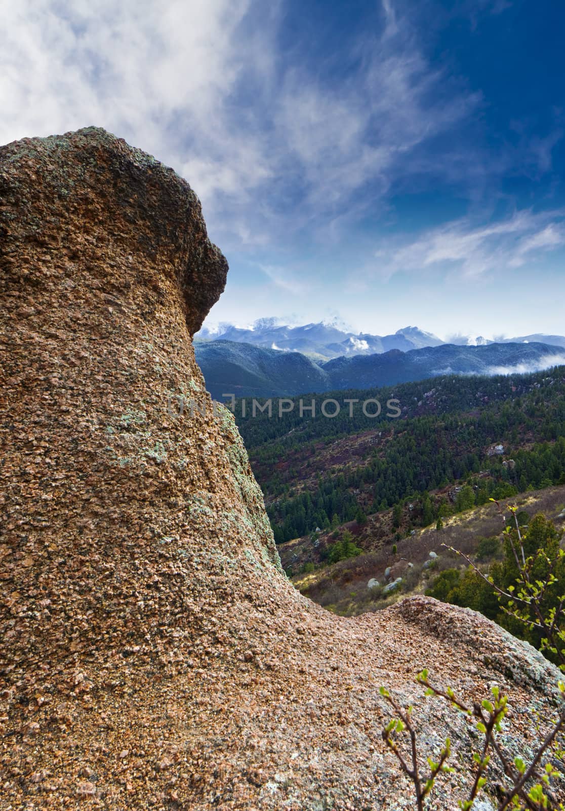 A large rock extends from the ground on a trail in Colorado with the snow capped Rocky Mountains in the background. 