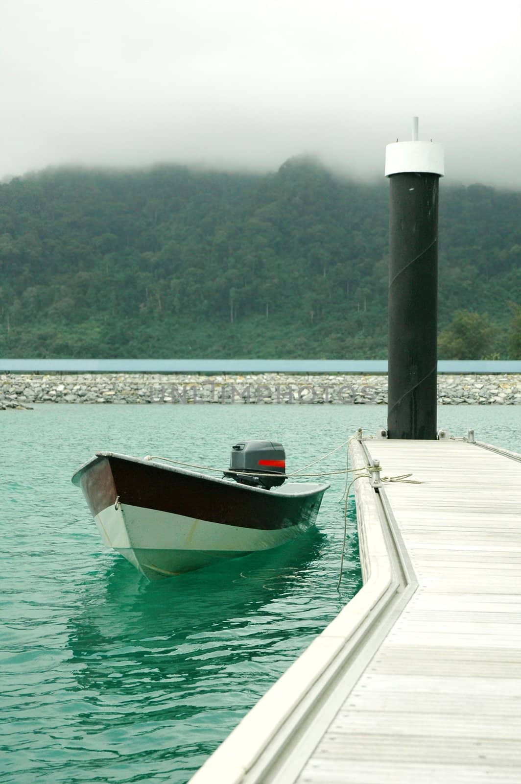 Boat at a wooden plank jetty against misty mountain backdrop