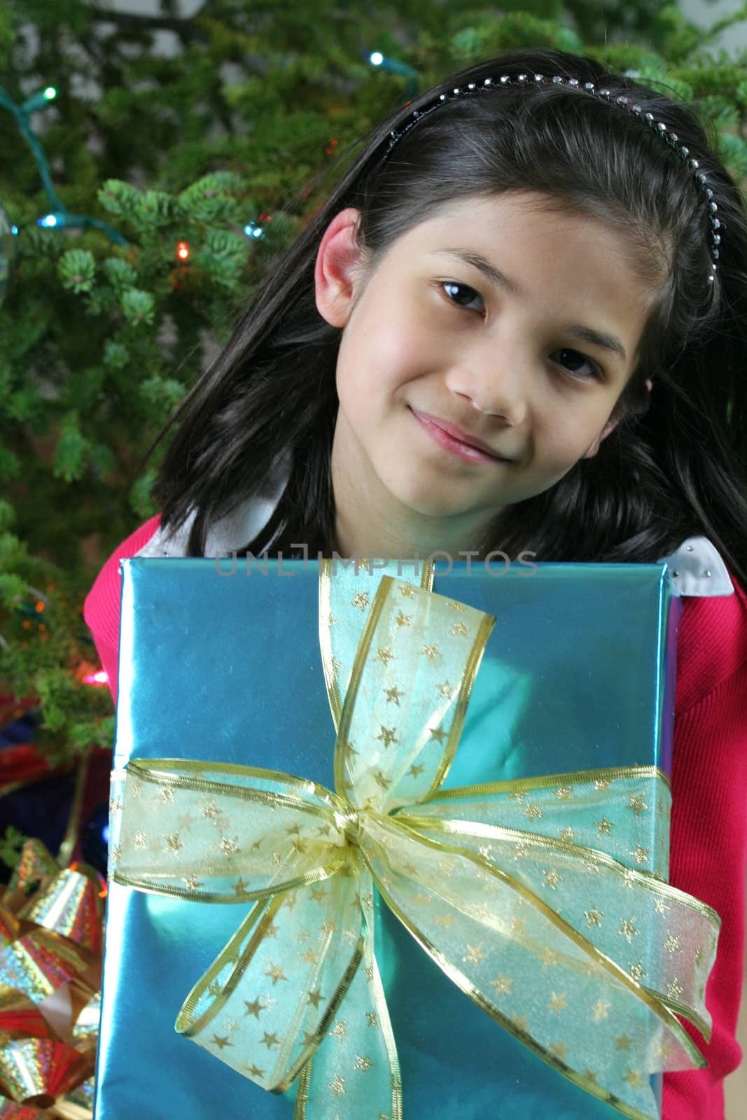 Happy little girl holding her Christmas presents by the Christmas tree. Part Asian, Scandinavian heritage.