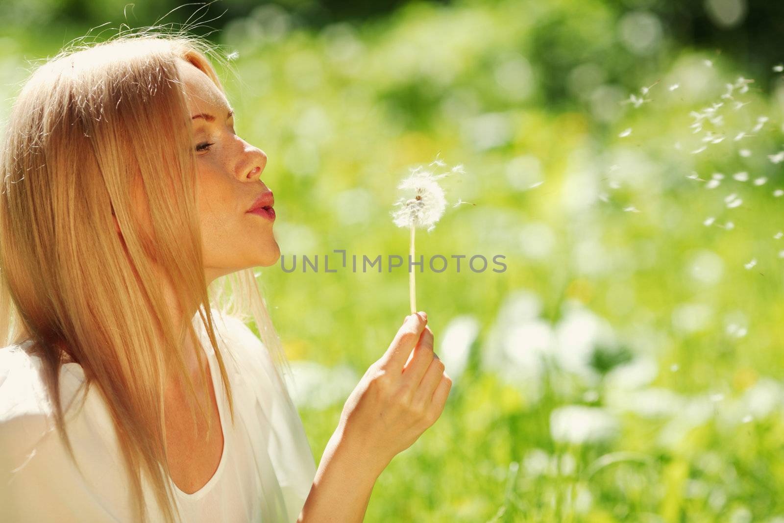 girl blowing on a dandelion lying on the grass