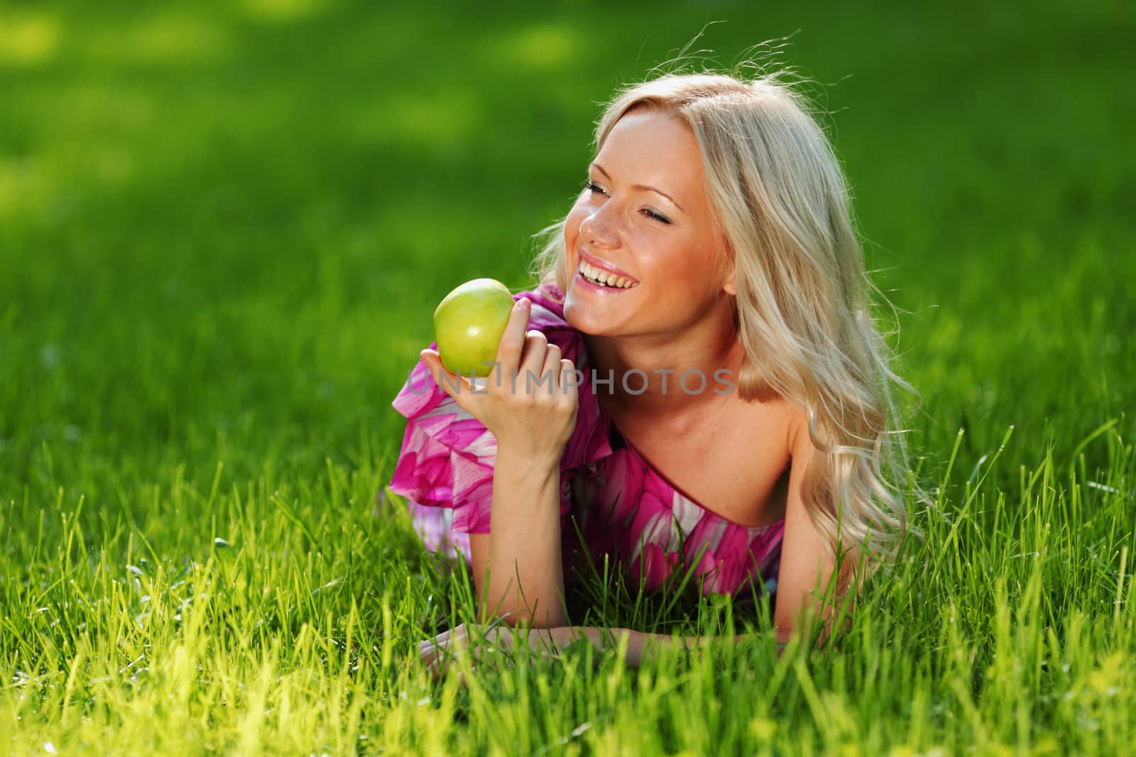 blonde holding an apple in his hand lying on green grass