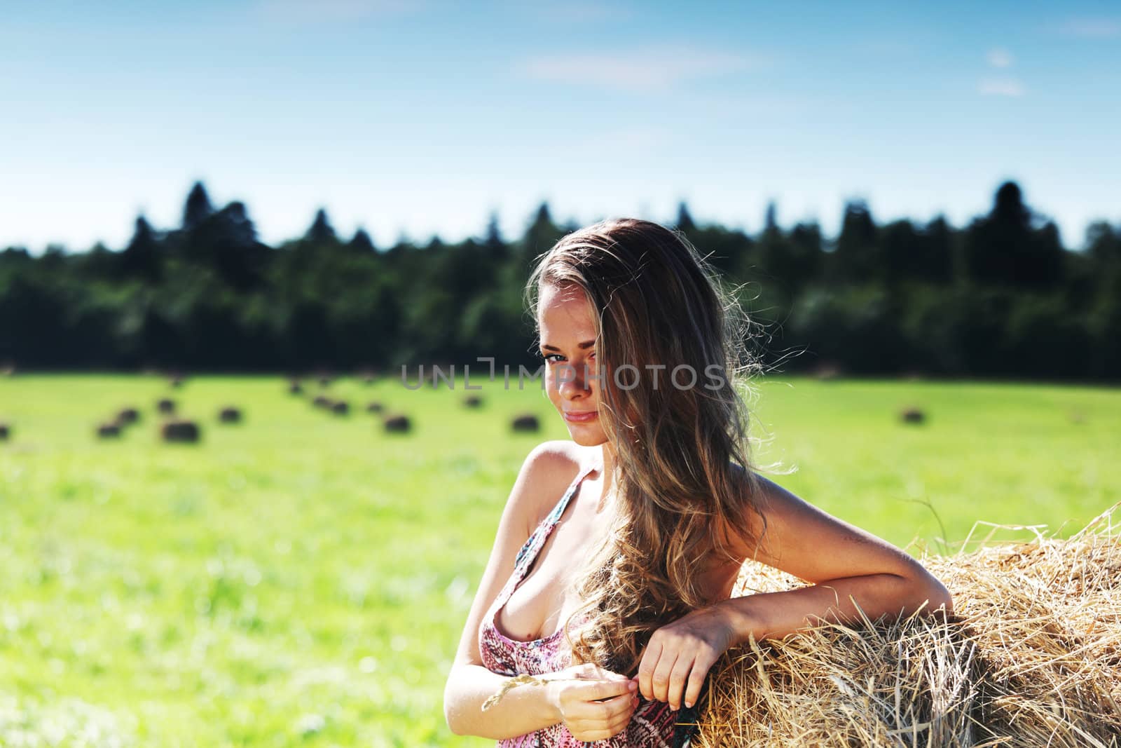 portrait of a girl next to a stack of hay under the blue sky