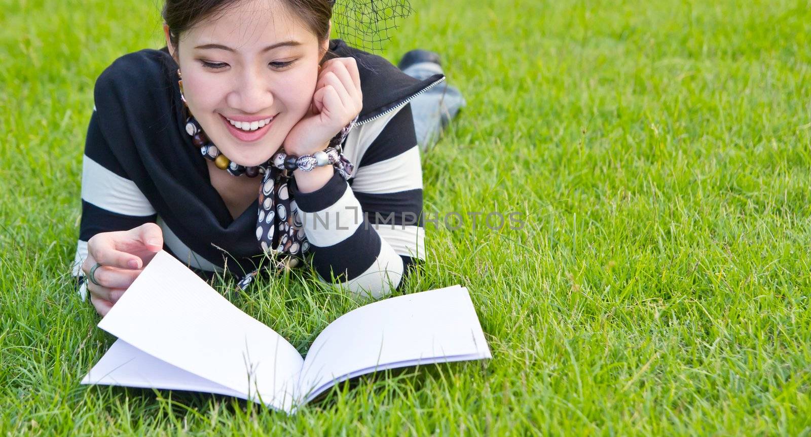 Asian woman reading notebook on the grass by Myimagine