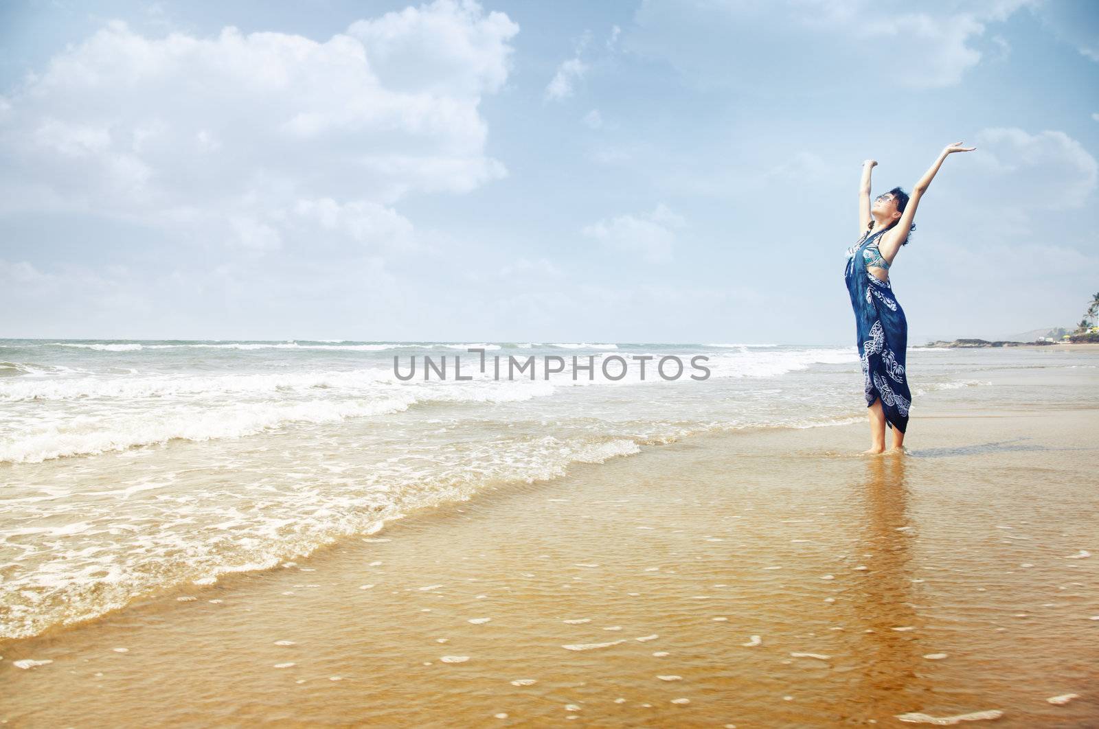 Happy lady standing in the water with hands up. Summer beach in Goa, India. Horizontal photo with vibrant colors