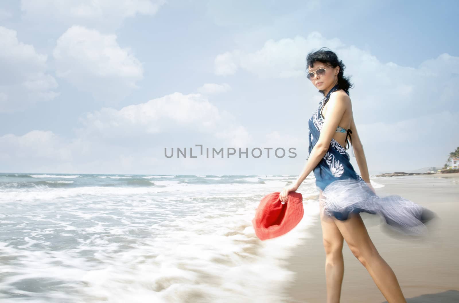 Lady with sunglasses and red hat going into the see. Motion blur added by the long shutter speed for dynamic effect