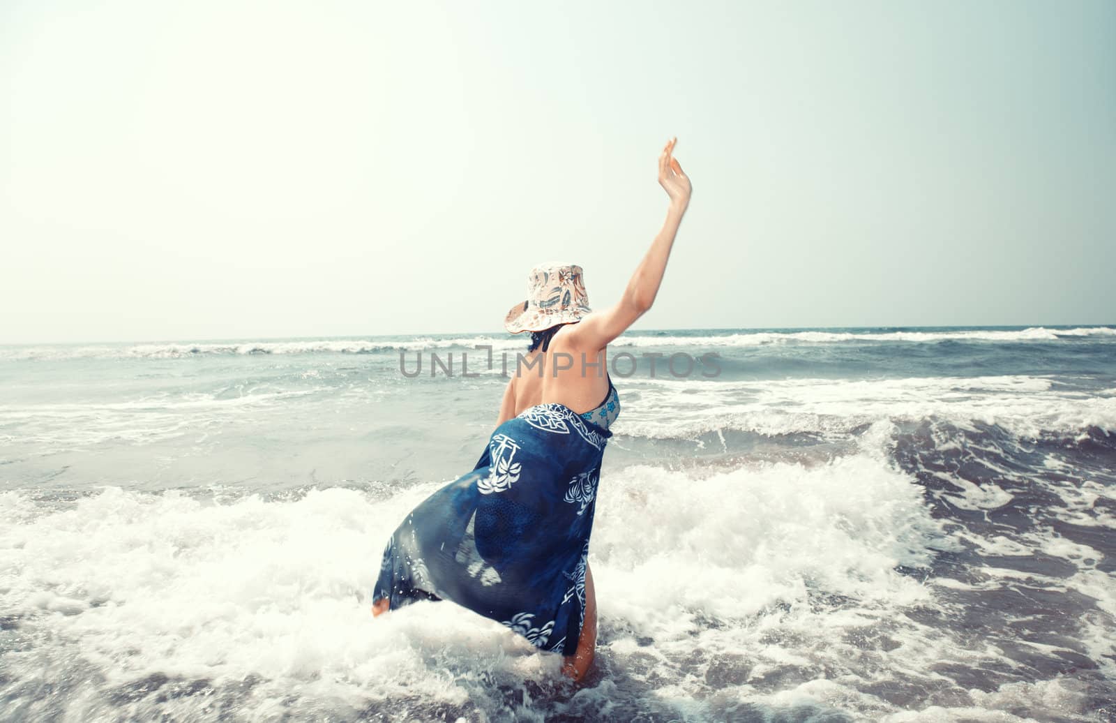 Happy lady in hat playing with waves at the sea