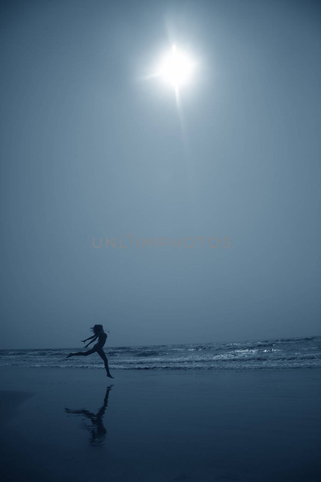 Silhouette of the lady dancing at the beach in deep dark night. Artistic blue colors toning added for coolness of the night