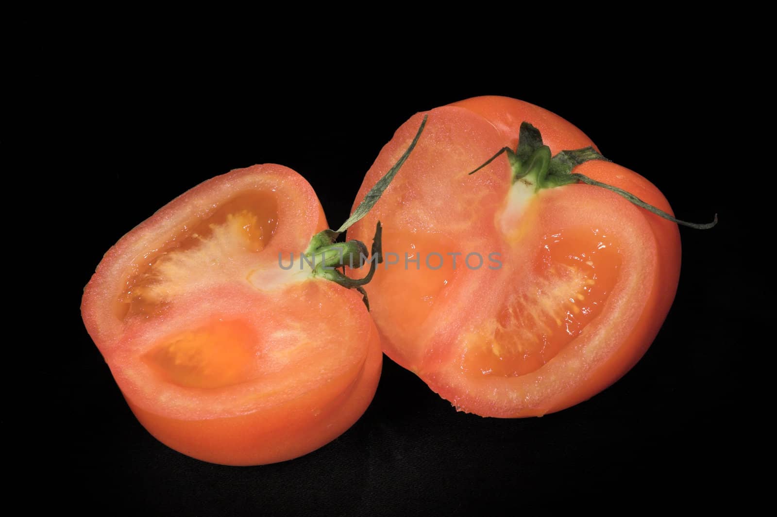 Two parts of the red cut tomato on a black background