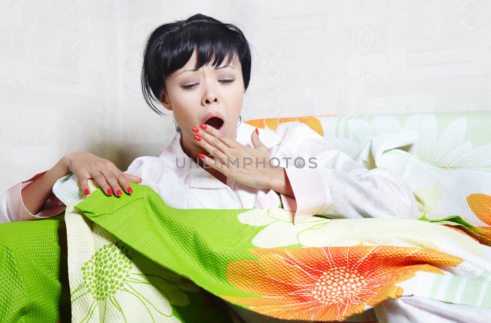 Yawning lady on the bed covered by colorful blanket