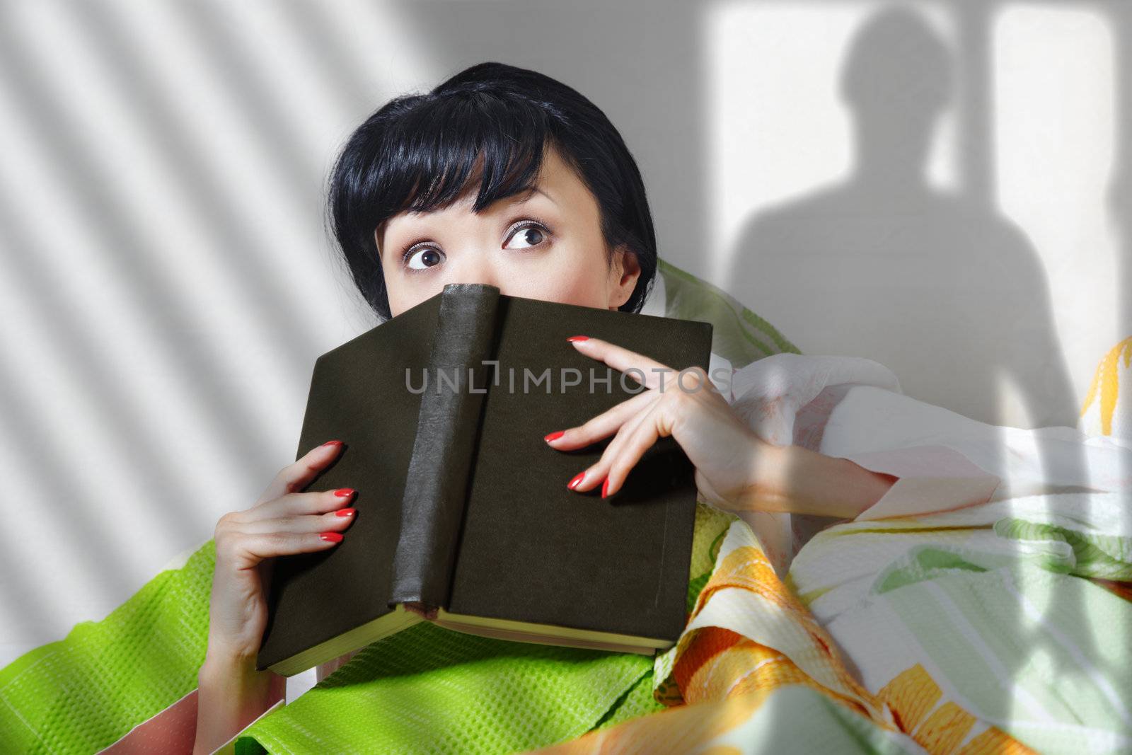 Afraid lady with book indoors looking to somebody. Shade of somebody is on the wall