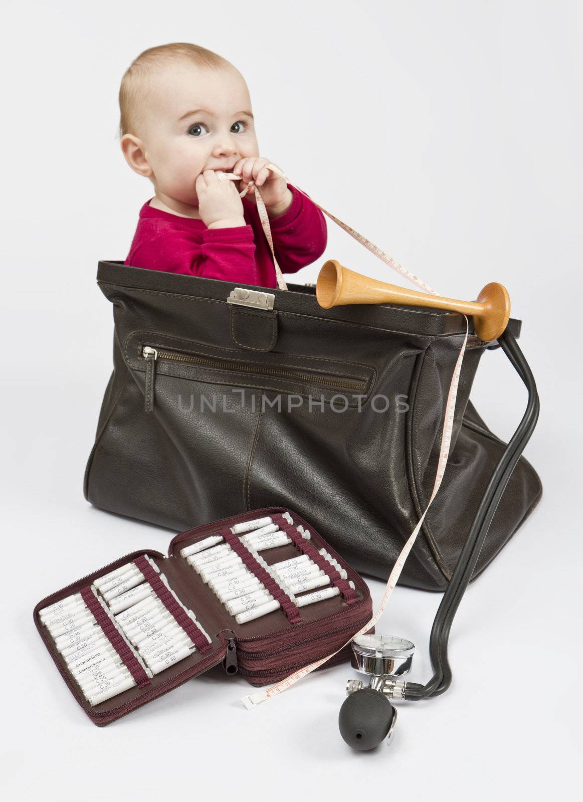 young child sitting in midwifes case with homeopathic globule , ear trumpet and measuring tape. No product names, just common names of homeopathic medicine.