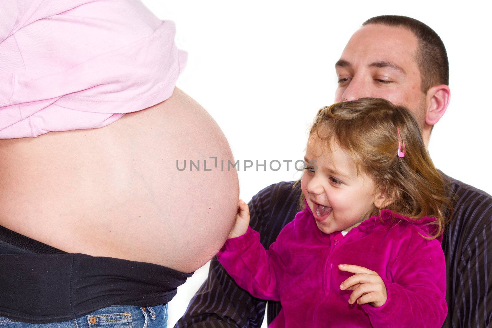 a young girl playing with her mothers pregnant belly helped by father
