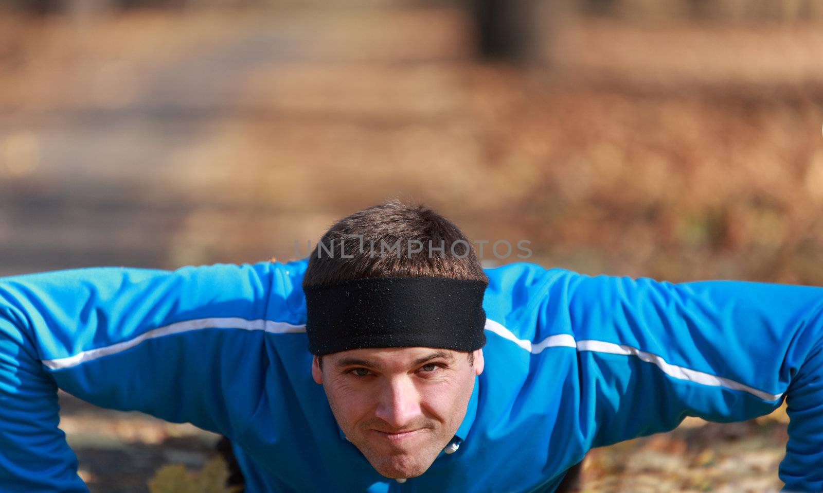 Portrait of a young man doing push-up outdoors in a park in autumn.