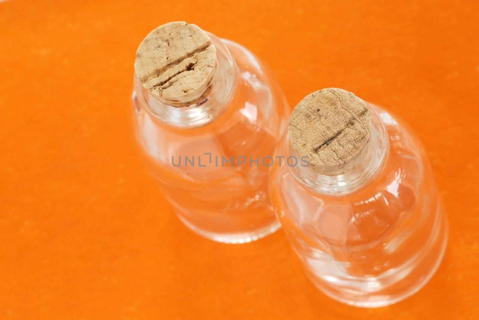 two small empty glass bottles closed with corks over orange background